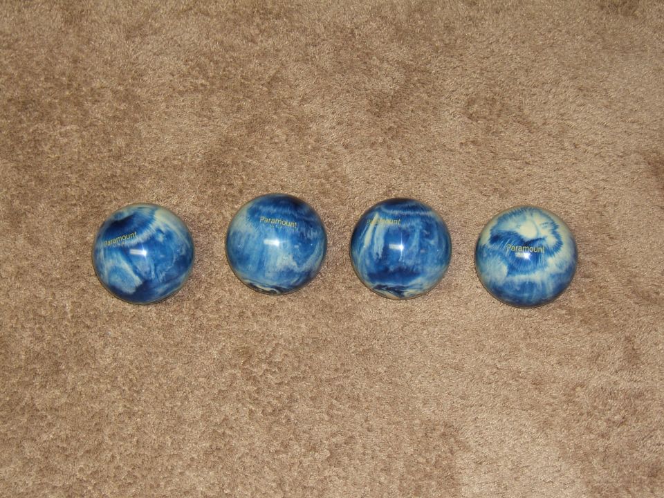 four blue and white swirl bowling balls on a brown carpet