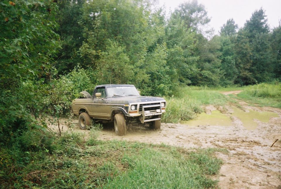 Muddy 1978 Ford F-Series pickup truck driving on a dirt track with puddles