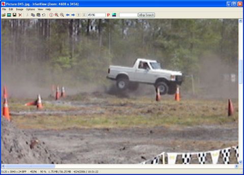 1989 Ford Bronco - A white pickup truck is airborne during an off-road event, navigating a course marked by traffic cones.