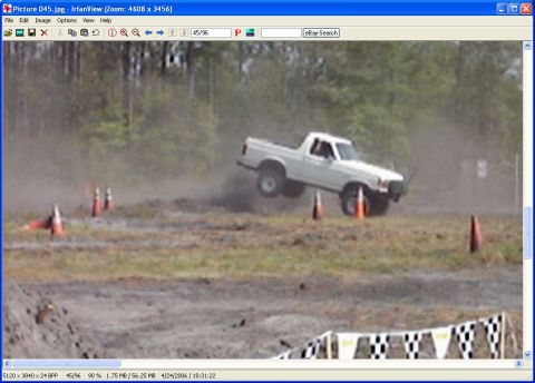 1989 Ford Bronco - A white pickup truck is captured mid-air during an off-road event, with cones marking the course.