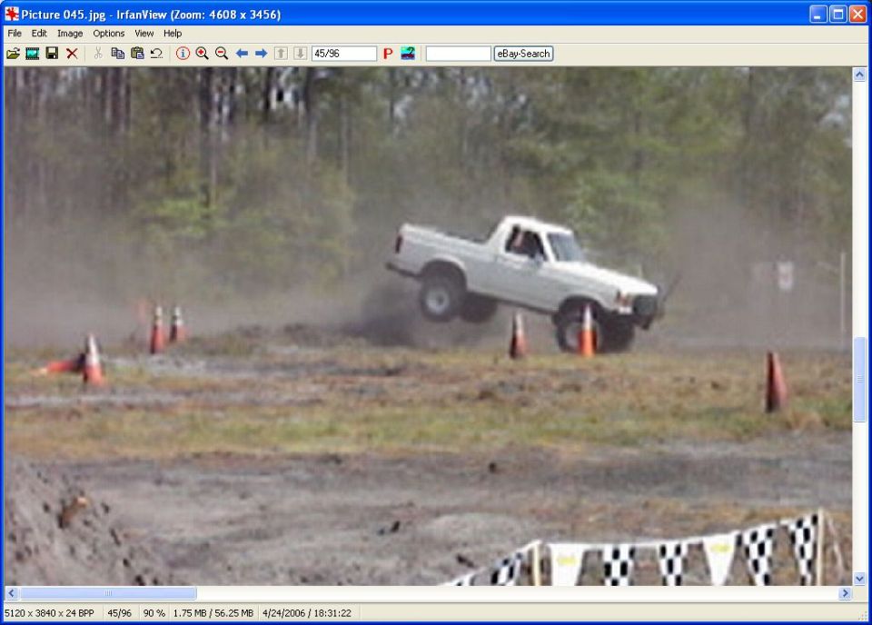 White pickup truck airborne over dirt track, driver visible, orange cones nearby