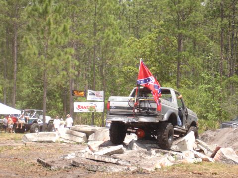 1989 Ford Bronco - This lifted truck navigates a challenging obstacle course, flying a prominent Confederate flag.