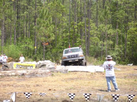 1989 Ford Bronco - A modified white Ford truck navigates an off-road course with spectators watching.