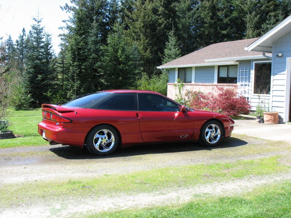 Red Ford Probe GT coupe parked in a driveway beside a house