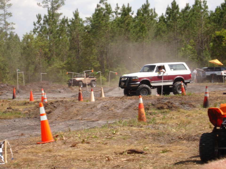 White and maroon Ford Bronco navigating an off-road course with orange cones. Another Jeep-like vehicle is in the background
