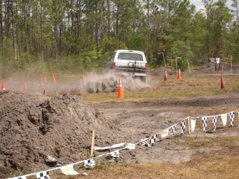 1989 Ford Bronco - A white SUV navigates a dusty off-road course with orange cones and checkered flags.