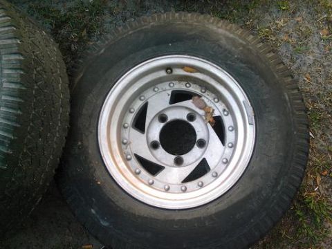 1986 Ford Bronco - A close-up view of two tires and their rims, one of which is a silver alloy wheel with a star pattern.