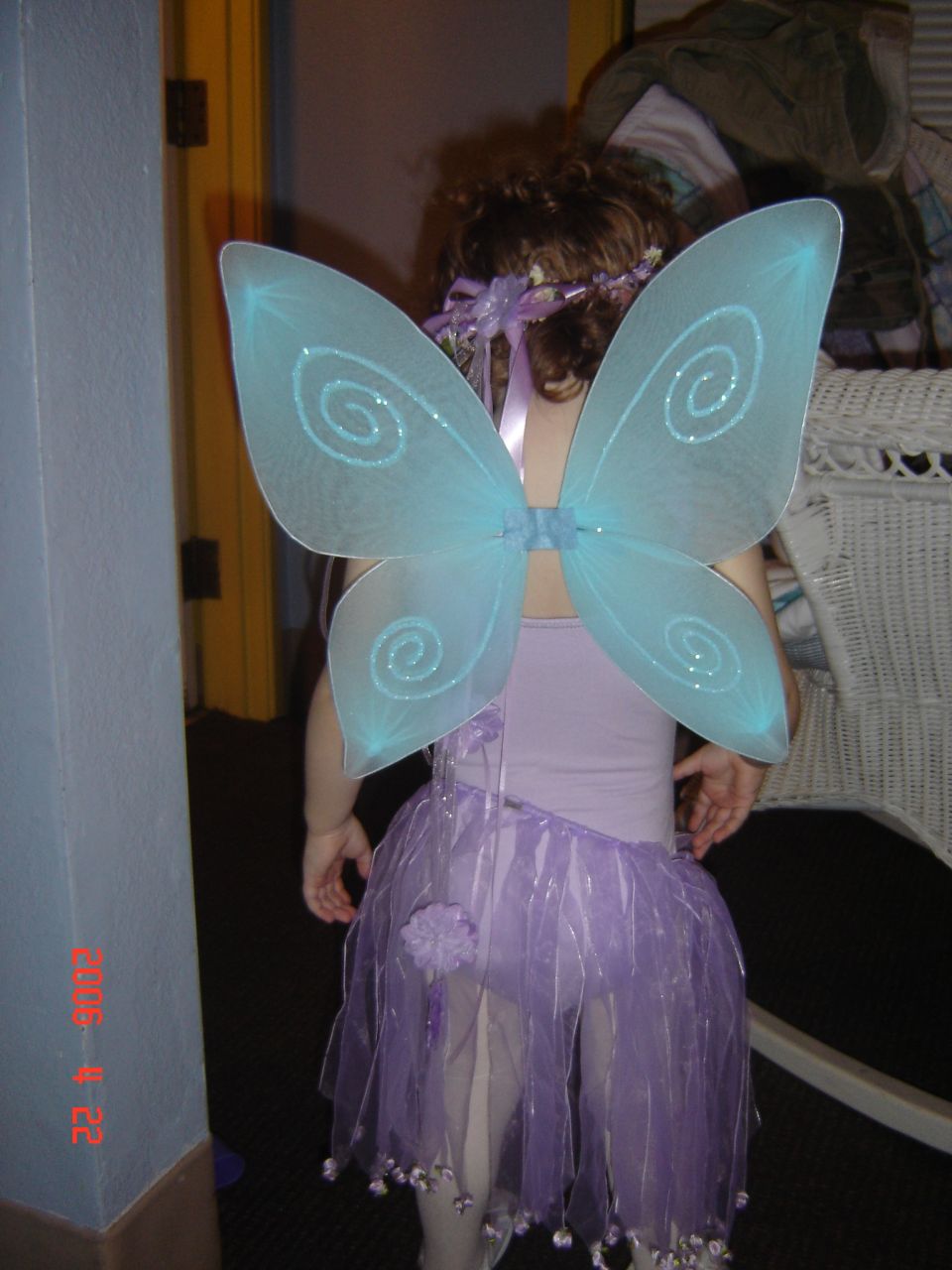 Child in a purple tutu and blue fairy wings, facing away from the camera