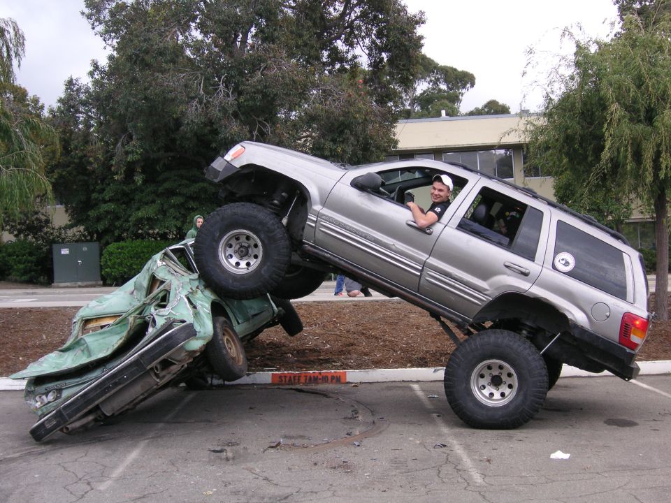 Silver 1999 Jeep Grand Cherokee crushing a green car, driver smiling