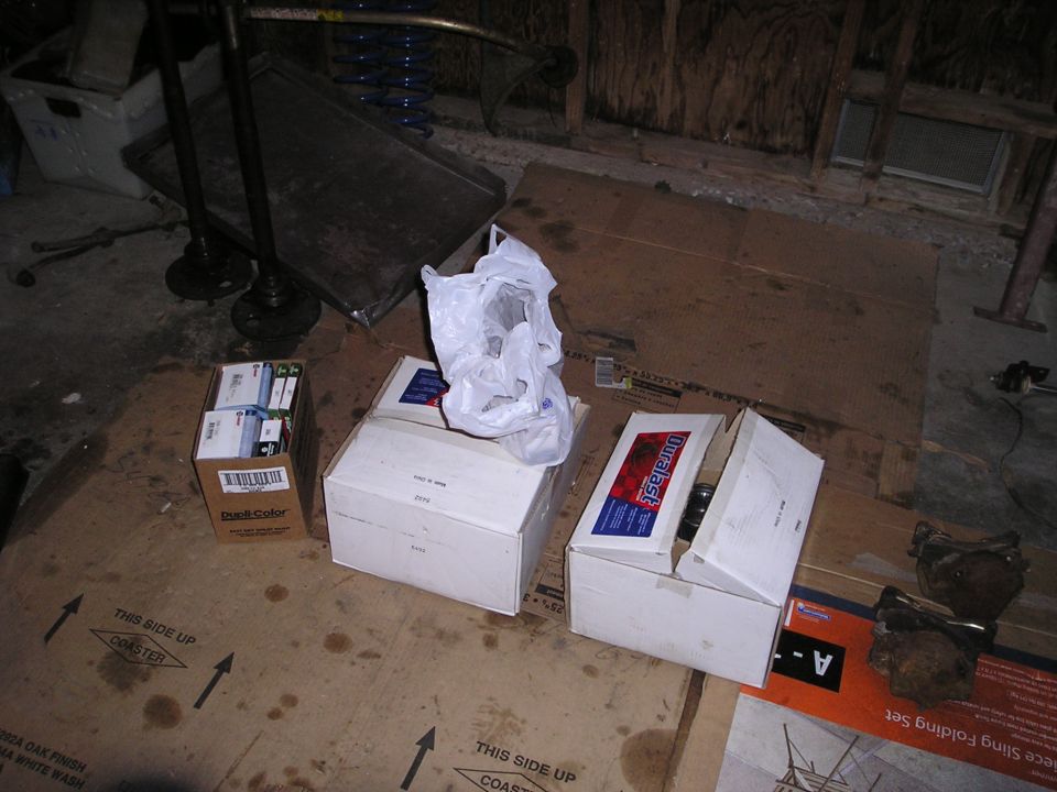 Boxes of parts and some rusty car components on a cardboard-covered floor