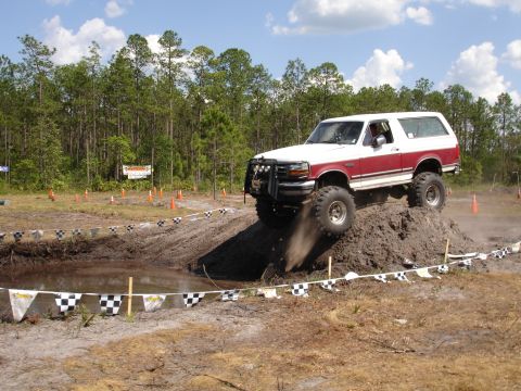 1989 Ford Bronco - Ford Bronco navigates a muddy obstacle course with a wooded background.