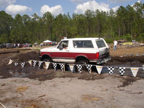 1989 Ford Bronco - A Ford Bronco navigates a muddy obstacle course during an outdoor event with spectators in the background.
