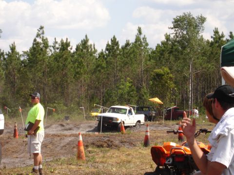 1989 Ford Bronco - Multiple trucks navigate a muddy off-road course with spectators present.