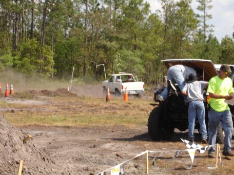 1989 Ford Bronco - A white pickup truck kicks up dust and mud as it drives through an off-road course.
