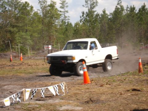 1989 Ford Bronco - Pickup truck navigates a dirt course with orange cones and checkered flags visible.