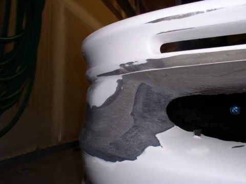1996 Ford Probe - Close-up of a white car bumper showing areas of body filler and primer, indicating repair work.