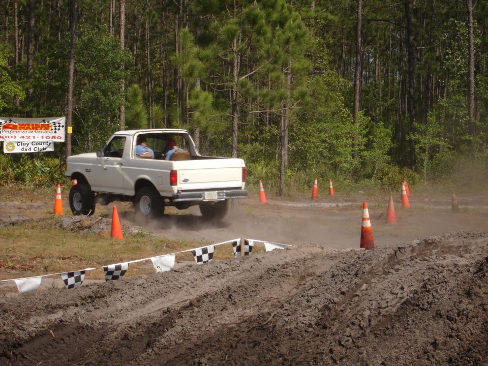 White pickup truck with a lifted suspension driving on a dirt track, kicking up dust