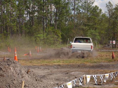 1989 Ford Bronco - A white 1987 Ford Bronco navigates a muddy off-road course, kicking up a cloud of dirt.