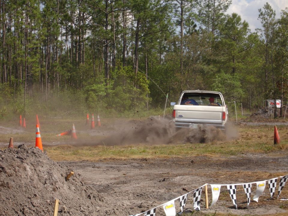 White 1987 Ford Bronco rear view, kicking up dirt on a muddy course