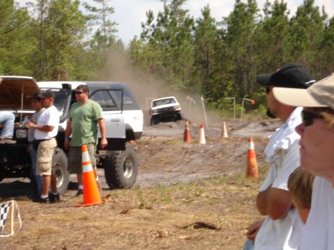 1989 Ford Bronco - Spectators watch as a vehicle navigates a muddy off-road course with several cones marking the path.