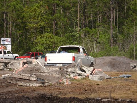 1989 Ford Bronco - A white Ford pickup truck navigates a rough terrain course with concrete obstacles.