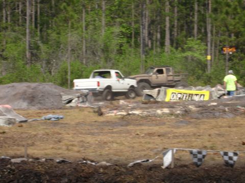 1989 Ford Bronco - Two trucks navigate a challenging off-road course with a sponsor banner visible.