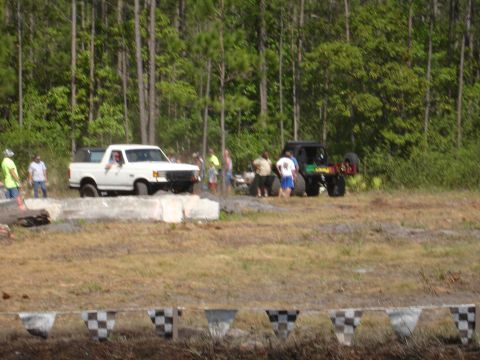 1989 Ford Bronco - A white pickup truck and a black off-road vehicle are parked in a grassy area with trees behind them.