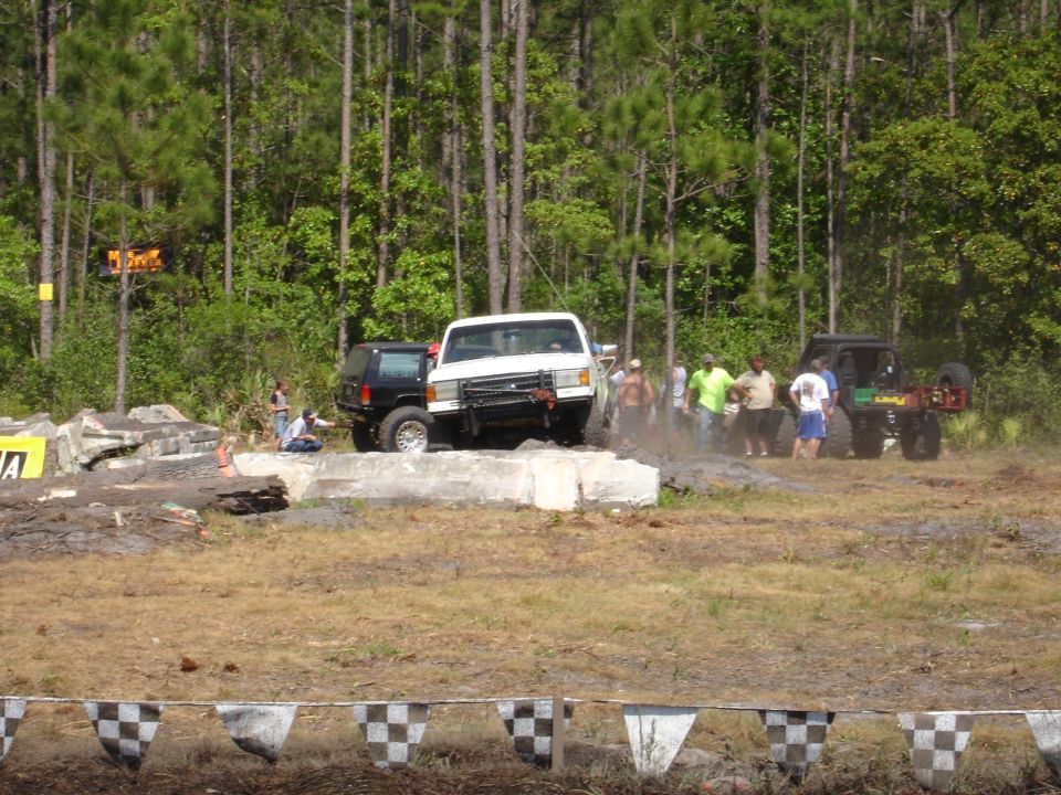 White pickup truck with a black SUV behind it, driving on an obstacle course