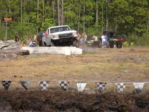 1989 Ford Bronco - A white pickup truck navigates an off-road obstacle course with spectators nearby.