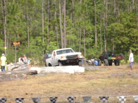 1989 Ford Bronco - A white pickup truck navigates an off-road course with spectators watching in the background.
