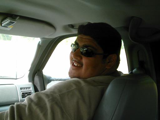 Man wearing sunglasses smiles while looking back from the passenger seat of a car