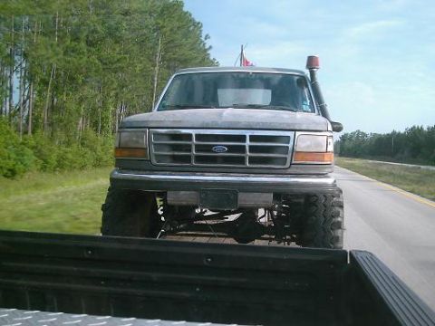 1986 Ford Bronco - A lifted gray Ford truck with a snorkel attachment is seen from behind, driving on a highway. The grille suggests a 1992 model year.