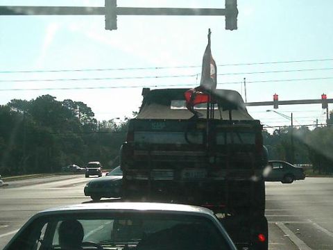 1986 Ford Bronco - A truck with a flag is seen from behind on a sunny day, with other vehicles on the road.