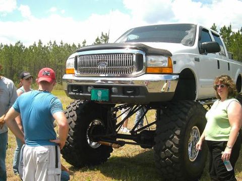 1986 Ford Bronco - White Ford F-250 Super Duty pickup truck is heavily modified with a lift kit and oversized tires.
