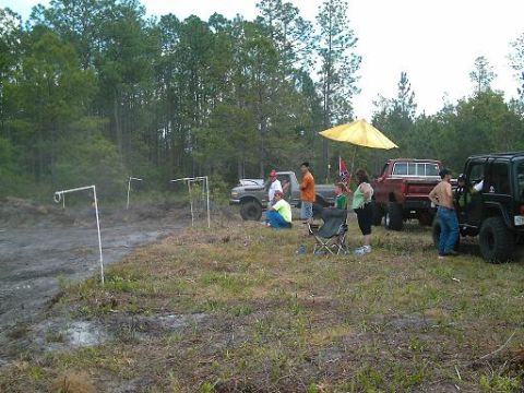 1986 Ford Bronco - Several people are standing and sitting around trucks and SUVs in a muddy, wooded area.