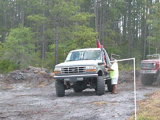 Light-colored lifted truck with a red flag, seen from a 3/4 front angle. Grille suggests 1987 model year