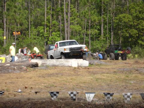 1989 Ford Bronco - Multiple off-road vehicles and ATVs gathered in a wooded area with spectators.