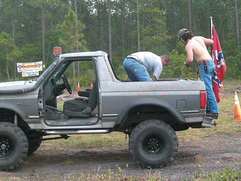 1986 Ford Bronco - A modified Ford Bronco is seen with its doors off, while two individuals attend to it, one holding a Confederate flag.