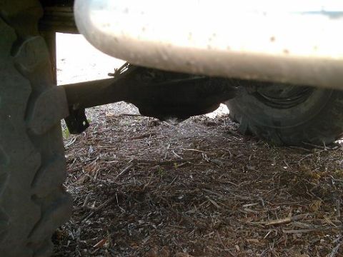 1986 Ford Bronco - The undercarriage of a vehicle, showing the rear axle and tires resting on a debris-covered surface.