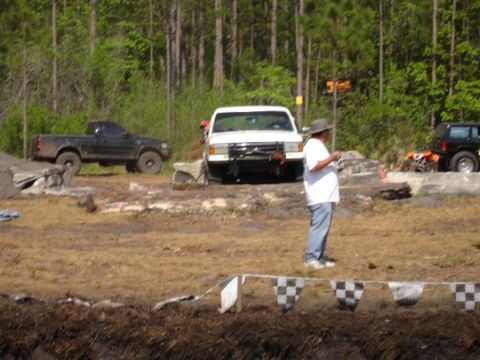 1989 Ford Bronco - A man stands near a white truck in an outdoor area with other vehicles and trees in the background.