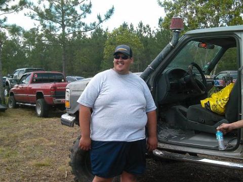 1986 Ford Bronco - Man poses next to a modified pickup truck, with another red Dodge pickup visible in the background.