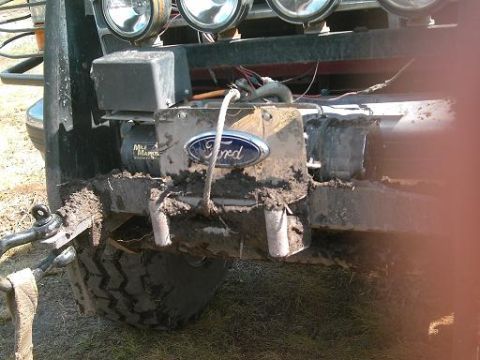 1986 Ford Bronco - Mud-caked front bumper of a 1986 Ford Bronco, a winch and auxiliary lights.