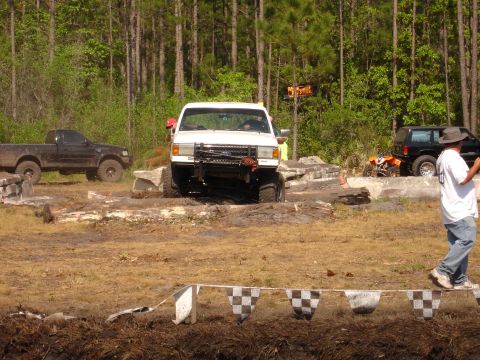 1989 Ford Bronco - Off-road vehicles navigate a muddy course with trees in the background.