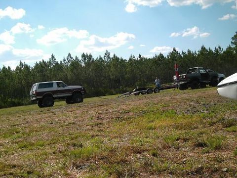 1986 Ford Bronco - Several vehicles are parked on a grassy field with a line of trees behind them under a partly cloudy sky.