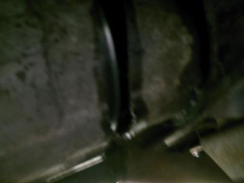1986 Ford Bronco - The underside of a vehicle is captured in this dimly lit photograph, revealing mechanical components and the chassis.