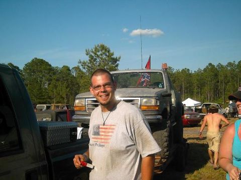 1986 Ford Bronco - A man smiles in front of a lifted truck with a Confederate flag flying.