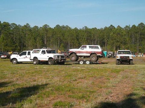 1986 Ford Bronco - A collection of off-road vehicles are gathered in an open field under a clear blue sky.