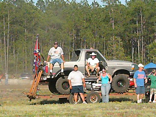 Lifted 1990s Ford F-Series truck on trailer with people around it. Confederate flag visible