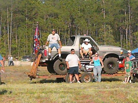 1986 Ford Bronco - A group of people gather around a heavily modified truck, with a confederate flag prominently displayed.