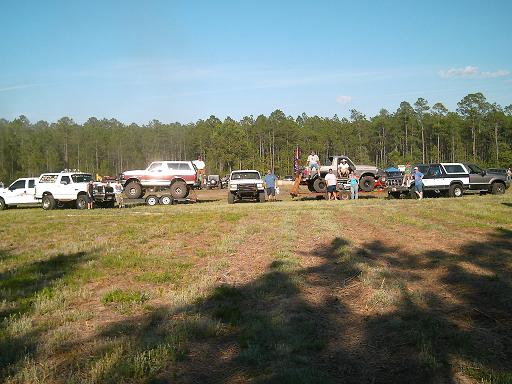 Several trucks and SUVs gathered in a grassy field with trees in the background